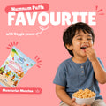 Happy toddler eating Manchurian Munchos baked puff snacks with Num Nam Manchurian Munchos bag and Numnam Puffs Favourite banner