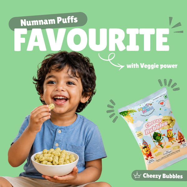 Happy toddler boy eating Cheezy Bubbles baked puff snacks from a bowl with Num Nam Cheezy Bubbles bag and Numnam Puffs Favourite banner on light green background