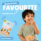 Happy toddler eating Tomaty Pumpos baked puff snacks with Num Nam Tomaty Pumpos bag and Numnam Puffs Favourite banner